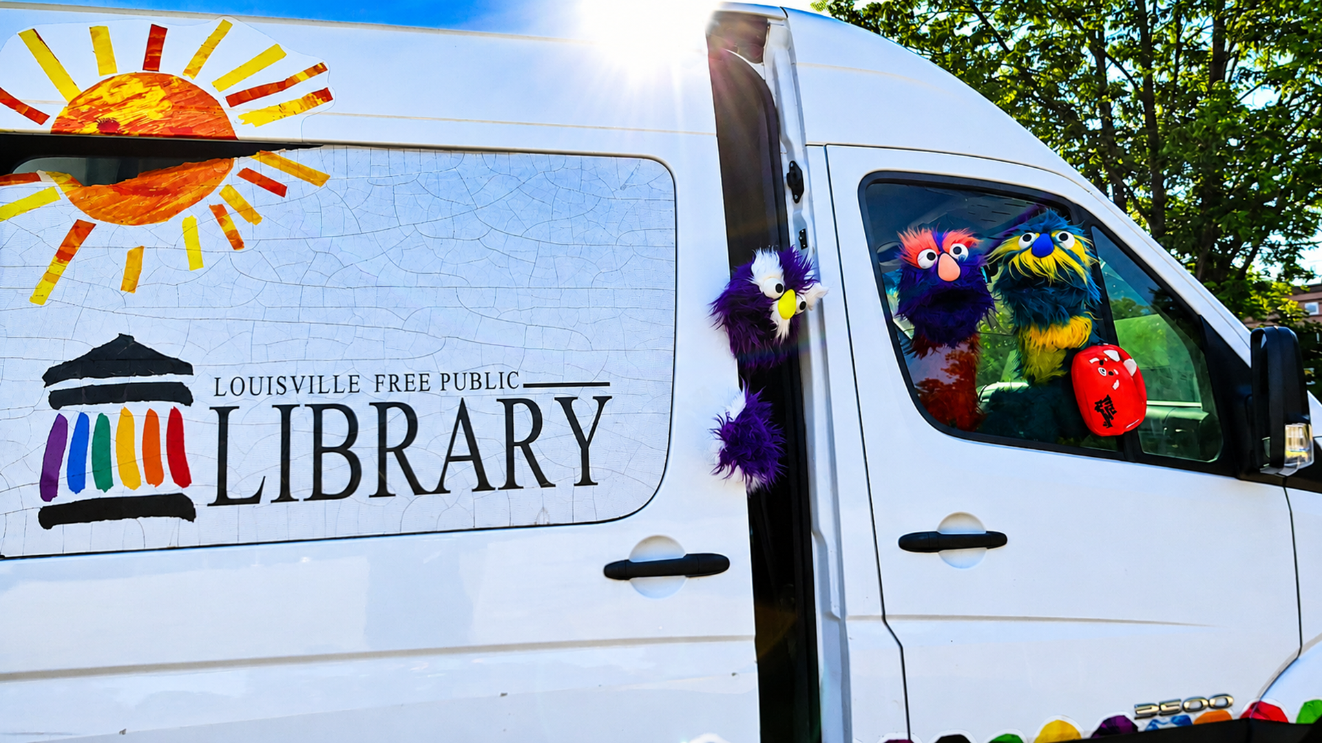 Colorful library van with fuzzy puppets peeking out and “Louisville Free Public Library” on the side.